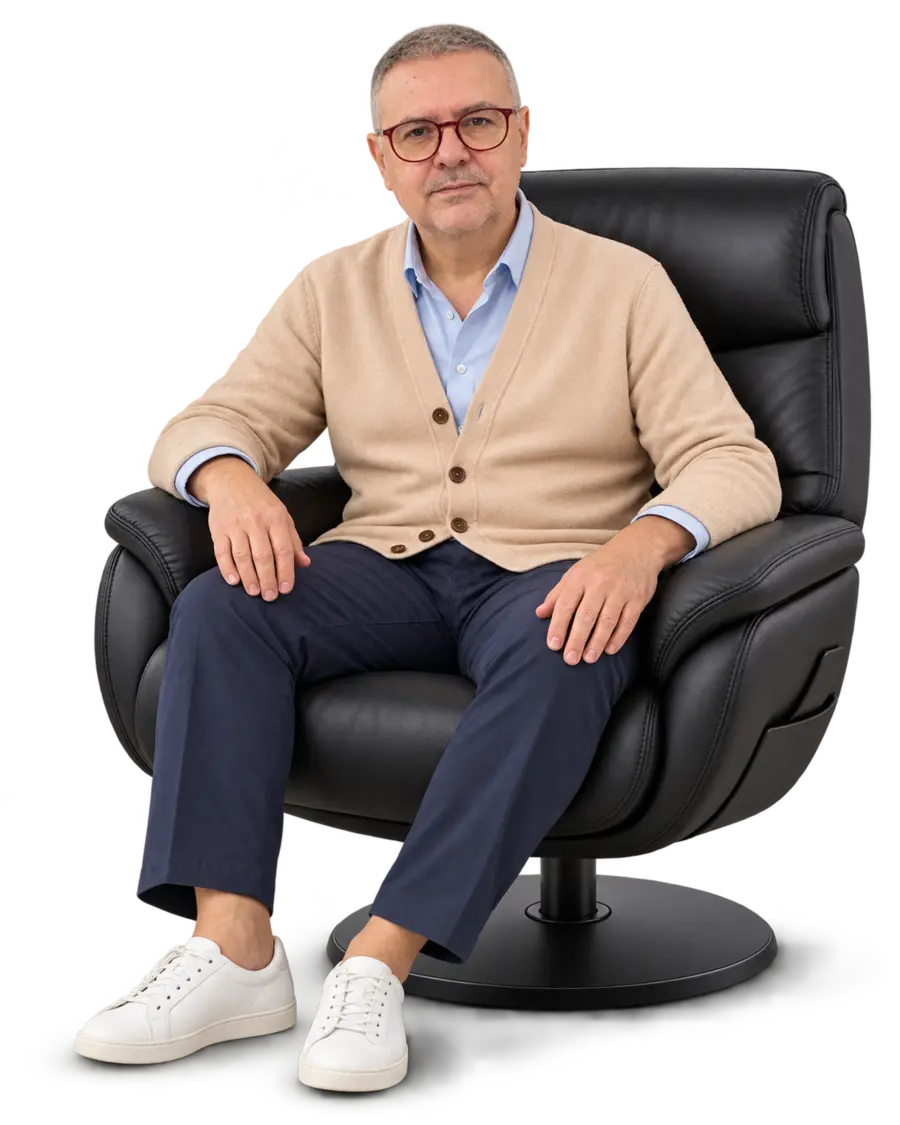João André com cardigan areia e camisa azul, sentado em postura de acolhimento na poltrona.